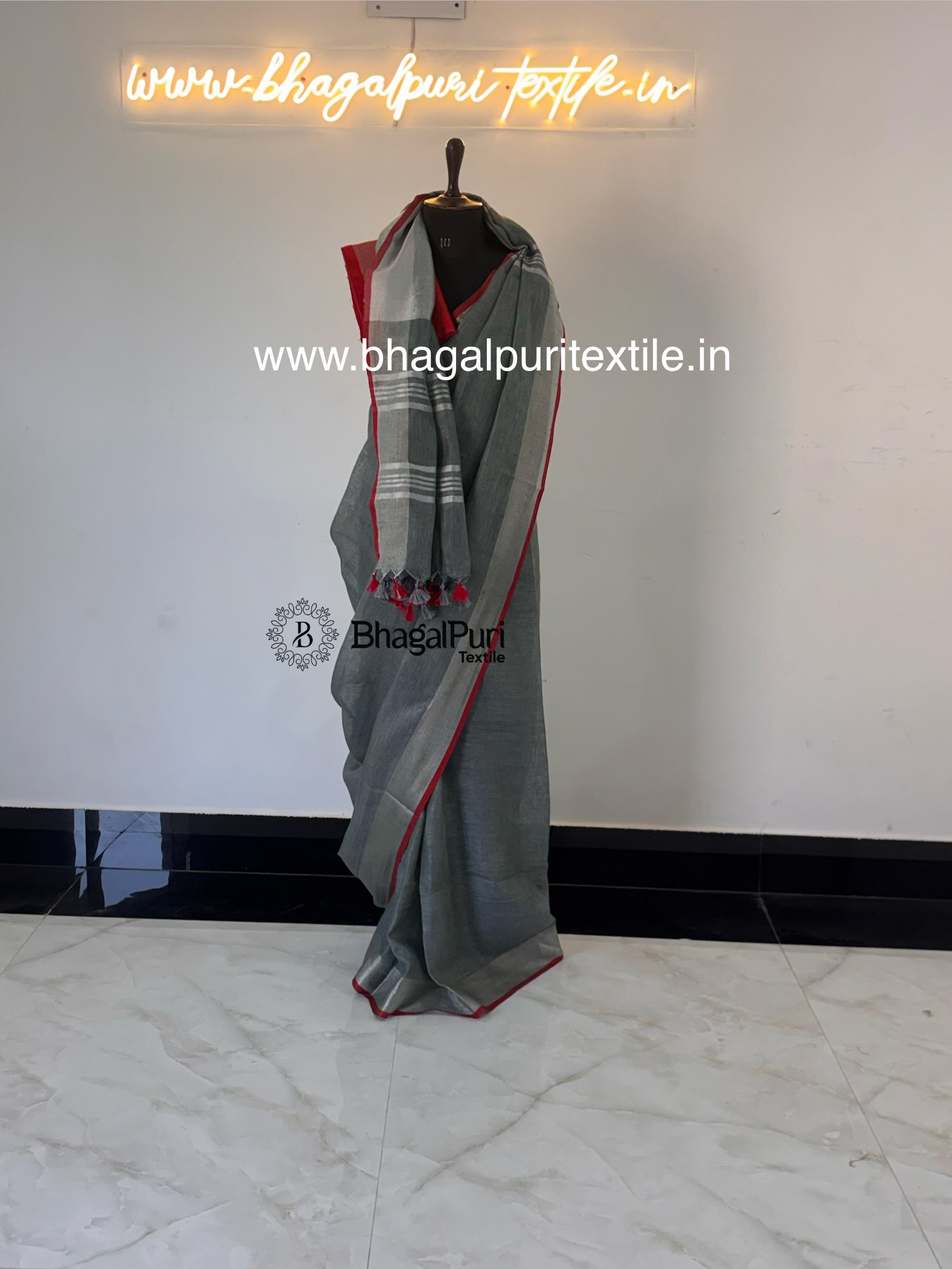 Stylish grey linen saree with red contrast border, tassel detailing, and elegant drape for women.