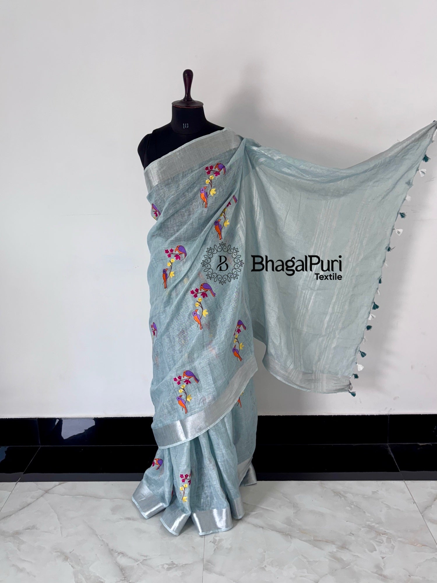 Light blue saree with floral patterns on a mannequin against a white background, branded 'BhagalPuri Textiles'.